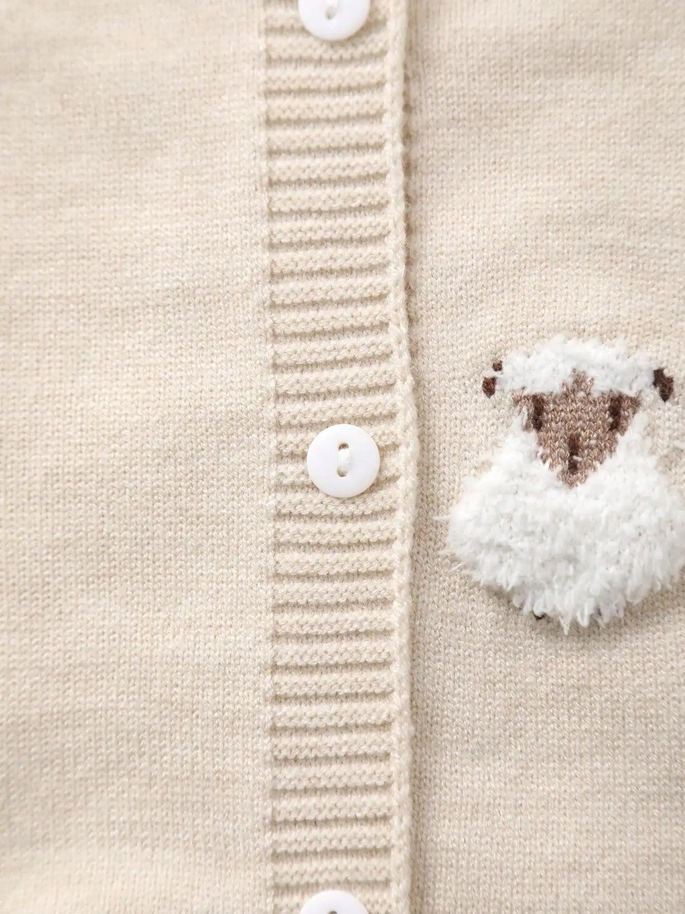 Close-up of a beige knitted cardigan with button details and a sheep-shaped button.