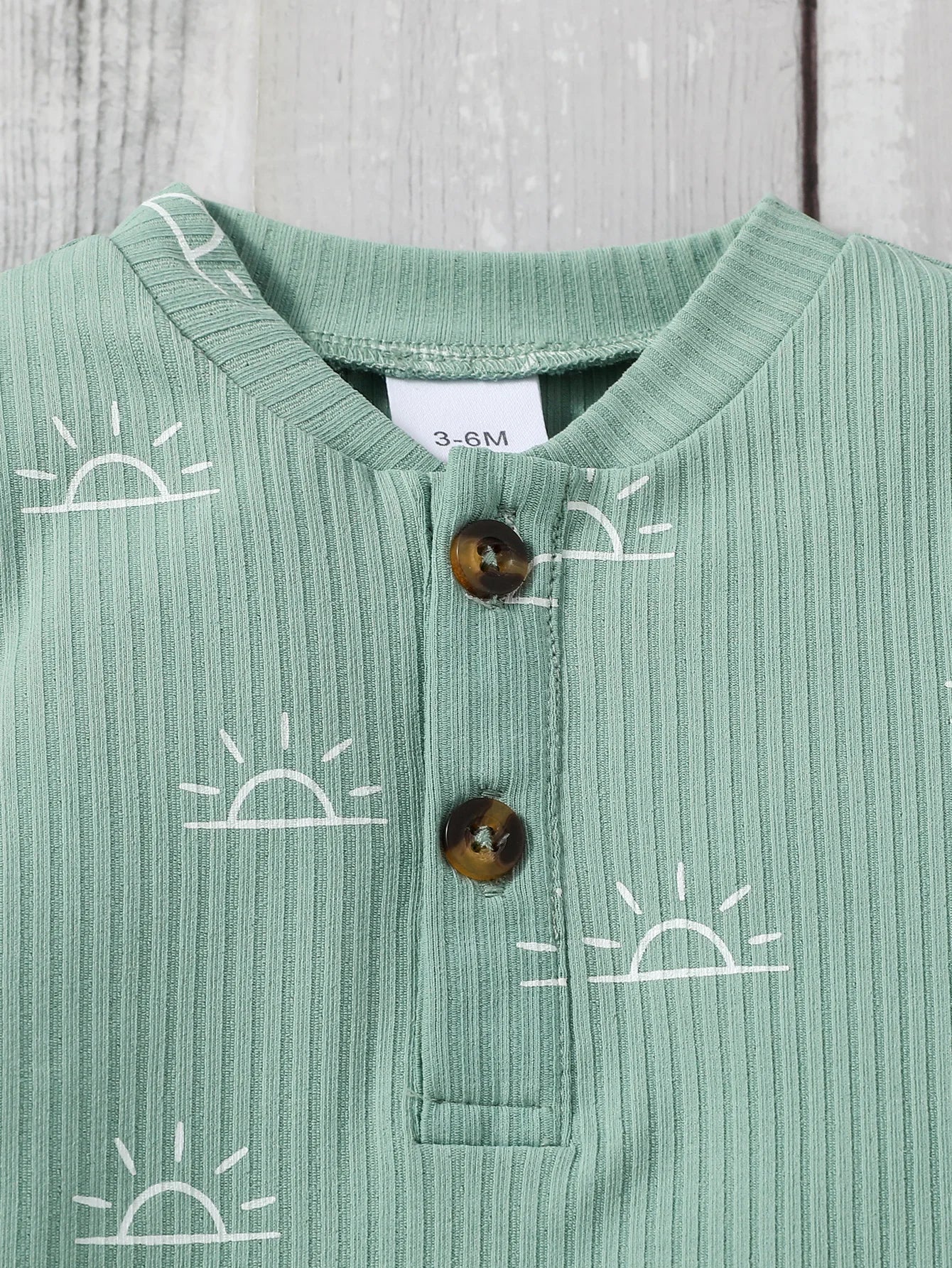 Green ribbed baby shirt with sun patterns and buttons 
