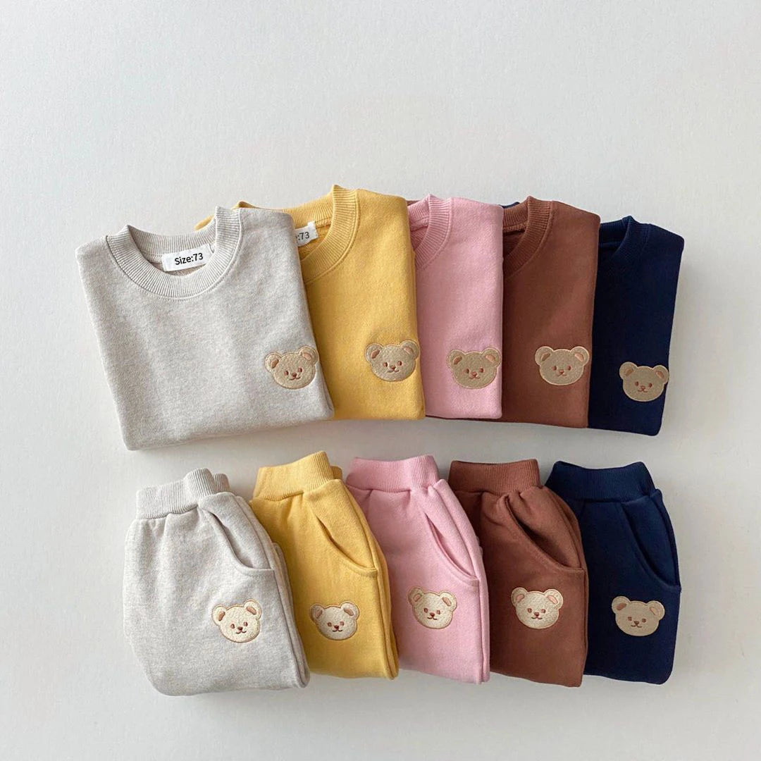 Set of folded sweaters and pants in various colors with bear embroidery 