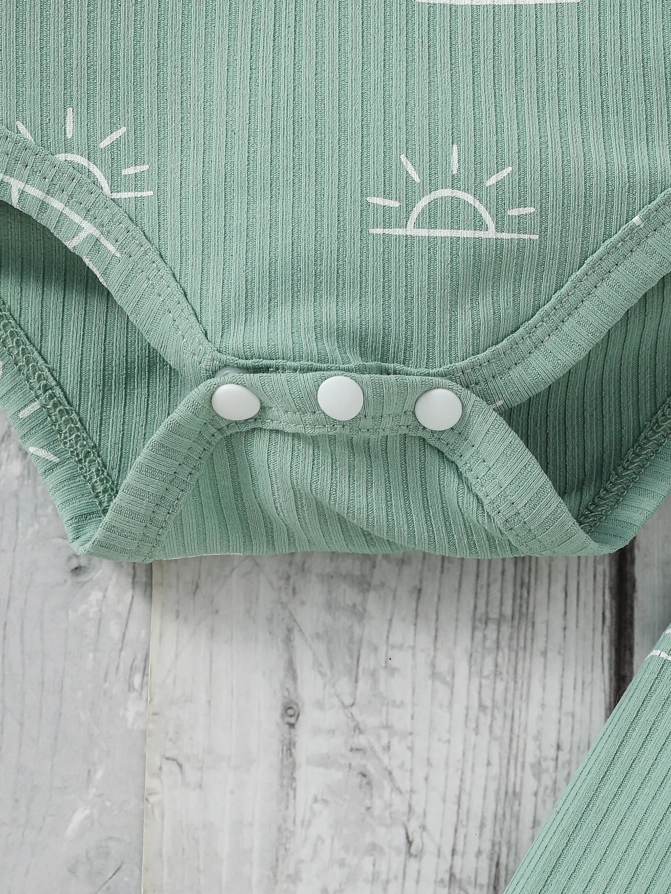 Green baby onesie with white buttons and a sun design 