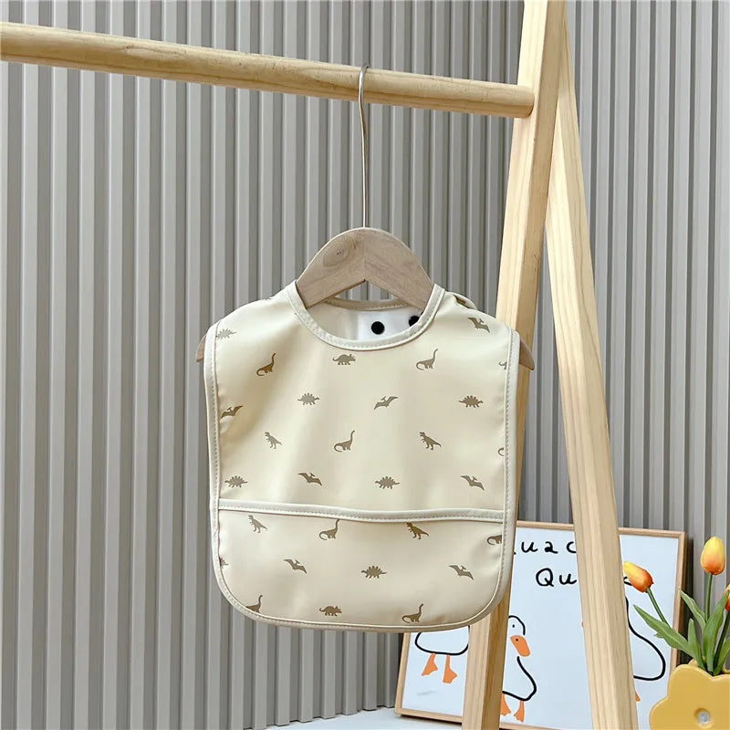 Beige bib with dinosaur pattern