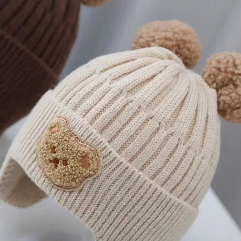 Beige knitted hat with a bear patch and two brown pom-poms 