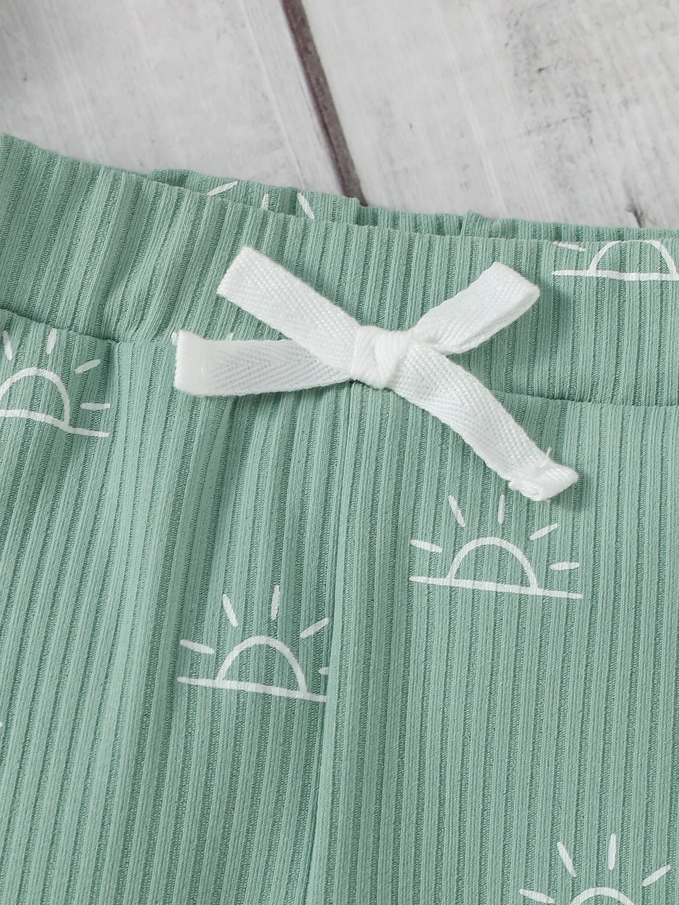 Green ribbed fabric with white sun patterns and a white bow 